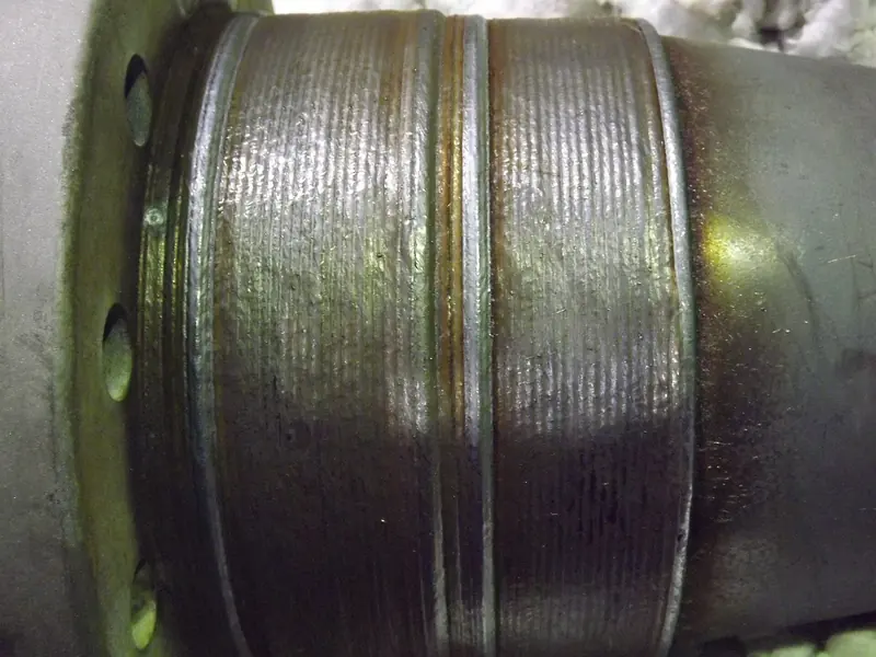 A close-up of ridged overlaid weld metal wrapped around a steel pipe next to a bolted flange.